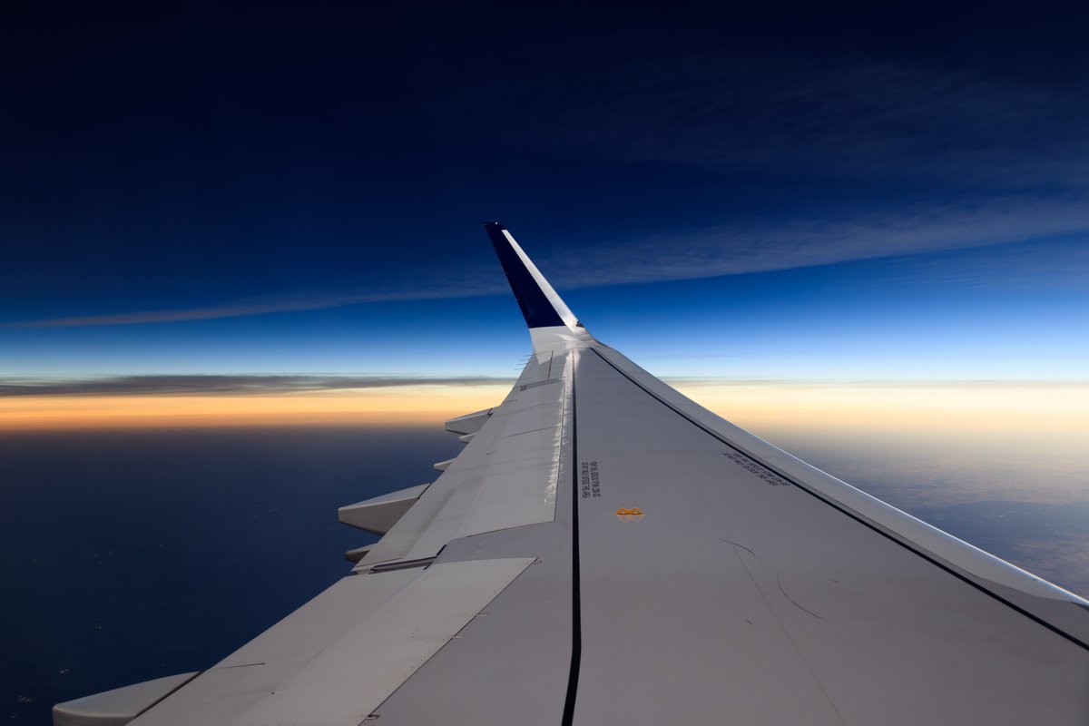 The land left of the wing (behind our flight path) in complete darkness (town lights visible) as the shadow of the Moon comes across during the solar eclipse. The wing and the land right of the wing (ahead of our flight path) are in sunlight. <a href="/Delta/">Delta</a> #DL1010, 1854Z April 8, 2024.