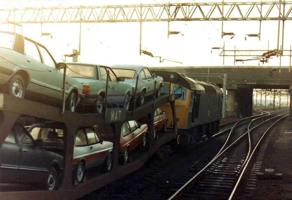 25254 at Nuneaton March 25th 1981 with its train of Ford cars being routed from the Down slow to the Coventry branch in order to reach Gosford Green. The MAT transporter wagon carries a selection of new Ford Capris, Cortinas and Fiestas. Dave Smith.