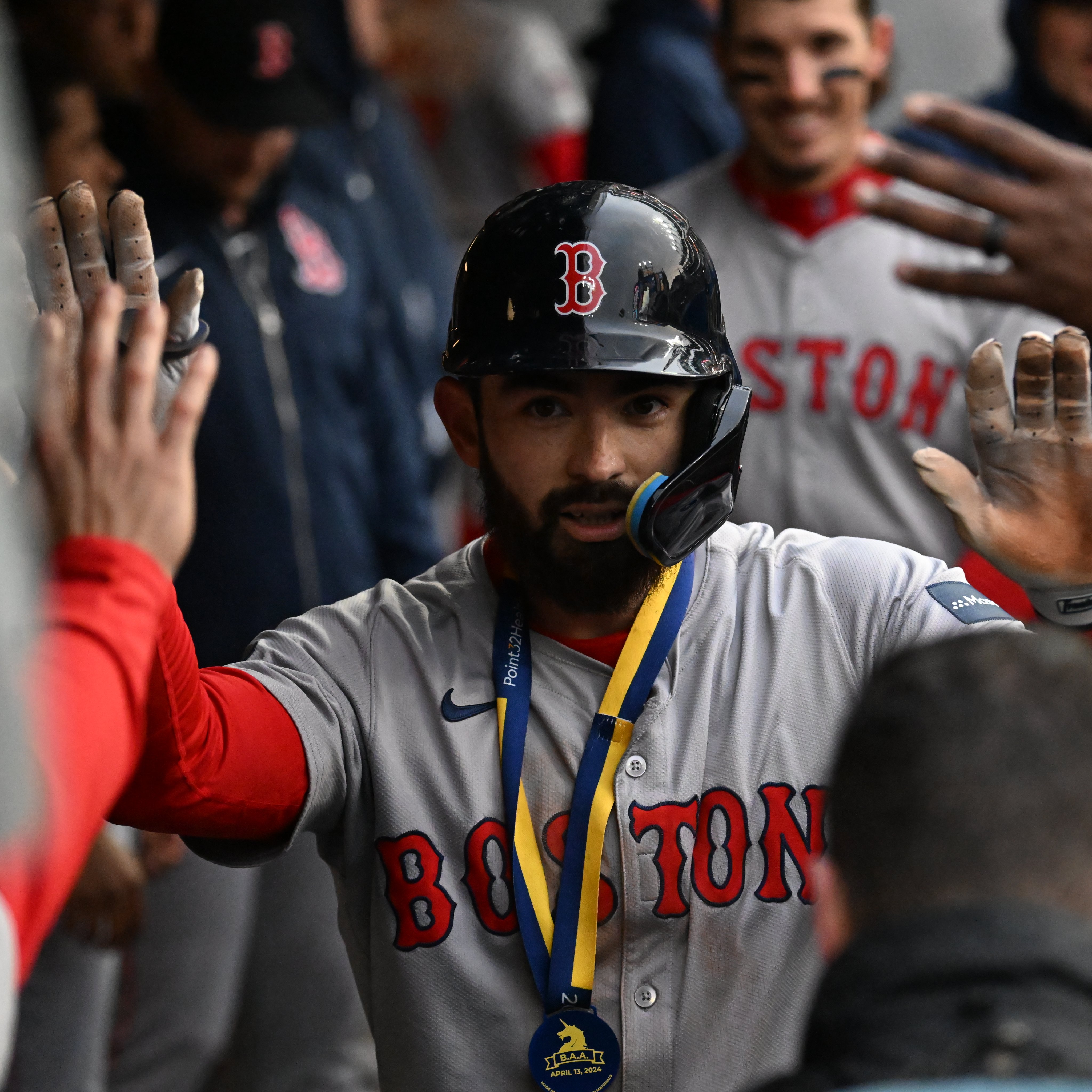 Connor Wong walks through dugout, both hands up high-fiving teammates, while wearing the Boston Athletic Association medal. 