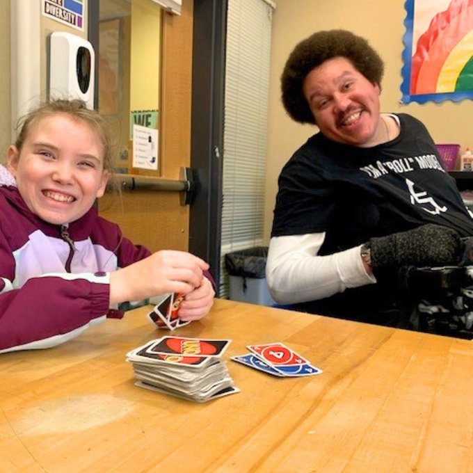 A volunteer and elementary school student smile for a photo while playing UNO at a table in a classroom