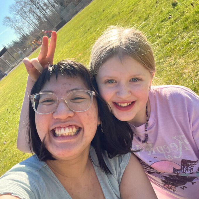 A volunteer and elementary schools student pose for a photo in a sunny grass field