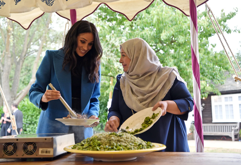 It is widely reported that the food tasting for the Grenfell cookbook had to be held in the palace grounds because MM could not be trusted inside. Regardless, here she is with her hair dangling in the food. Eugh!!