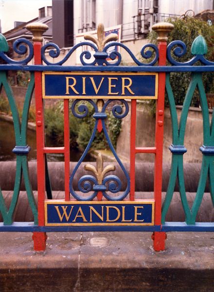 Wednesday Archive Day. This picture was taken at Wandsworth High Street Bridge and shows the bright painted iron work celebrating the River Wandle. Sadly today is now painted black.