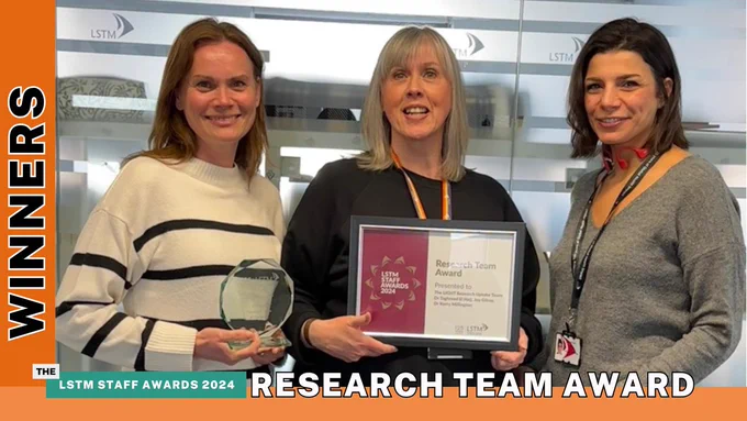 Kerry Millington, Joy Gilroy and Taghreed El Hajj standing together in LSTM offices. Kerry is holding a glass trophy and Joy is holding a framed certificate. All are smiling.