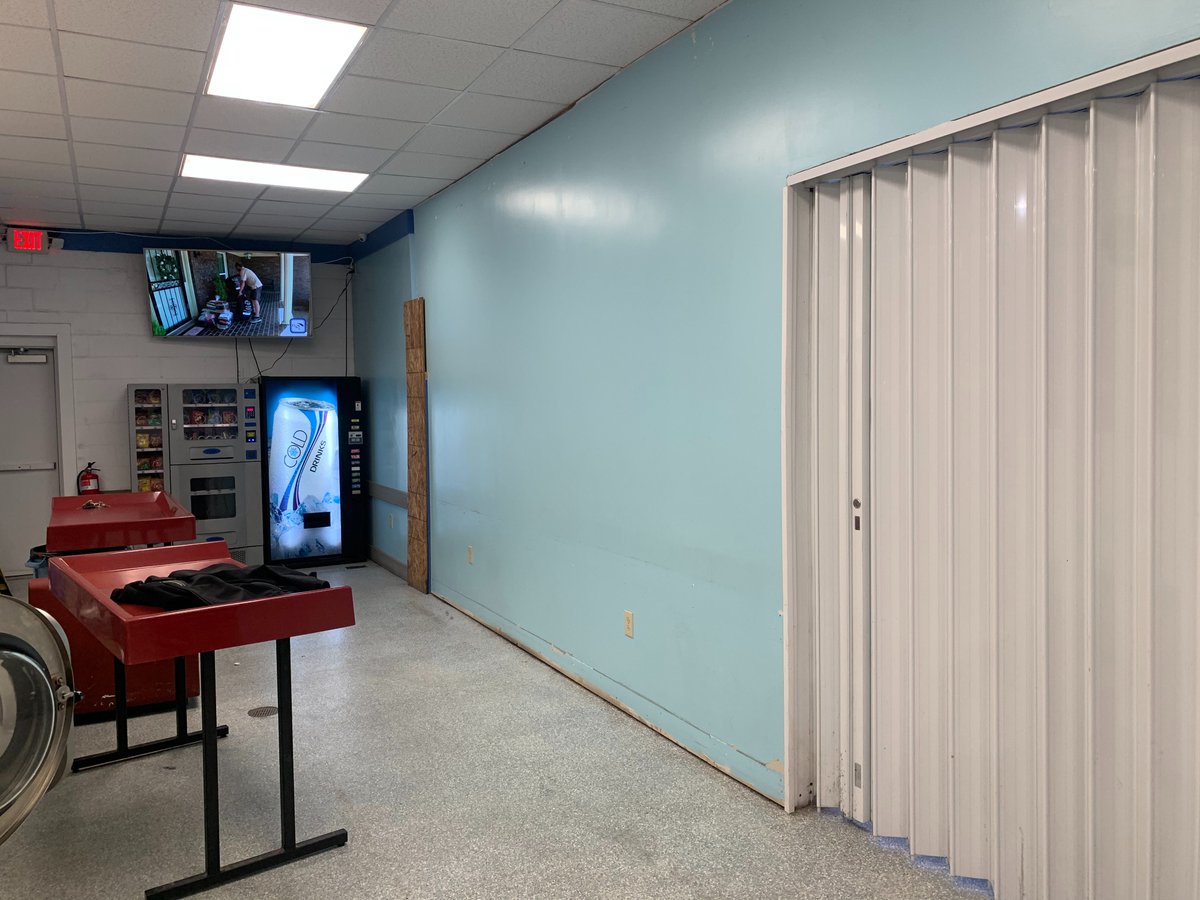 KenBarrettHQ's tweet photo. I originally left this area of the store to add WDF.

I sold off my WDF at another location and have no interest in that part of the business anymore so I put the space to better use.
The black box under the folding table contains hookups for another bulkhead.

The white door is a hurricane shutter from Alutech dot com. I had the same one cover the WDF counter at my other laundromat. I'll show more details on that in a future post. I leave the bottom guide off the door so there is no trip hazard.(It's in the back room if someone is looking to purchase one.

The store flooring is Epoxy (not a fan), the brown area is the original  terrazzo floor and the blue is where I stained some unfinished concrete. Gives a bit of a beach effect now.

The mural was done by a local artist over 2 days for $500. It was finished in early 2020 but we didn't remove the wall for over a year due to the 'Rona.

Also I install 1/2" OSB under all of the drywall. Makes it easier to hang things if needed and as my mentor once said, "I may find knuckle marks but I won't find a hole"

If you build a new store you don't have to utilize every square inch. If possible leave some options for the future.