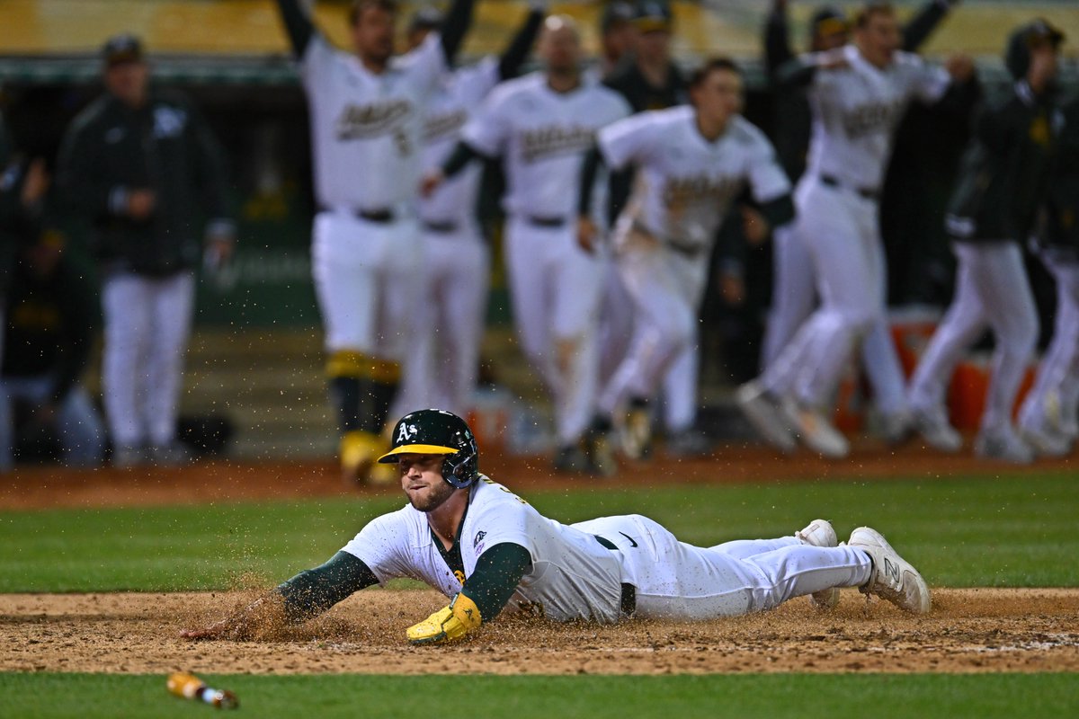 Oakland Athletics' Max Schuemann (12) slides into home plate to score the game winning run on a single hit by Oakland Athletics' Lawrence Butler (4) in the 10th inning of their MLB game at the Coliseum in Oakland, Calif., on Friday, April 12, 2024. #rootedinoakland