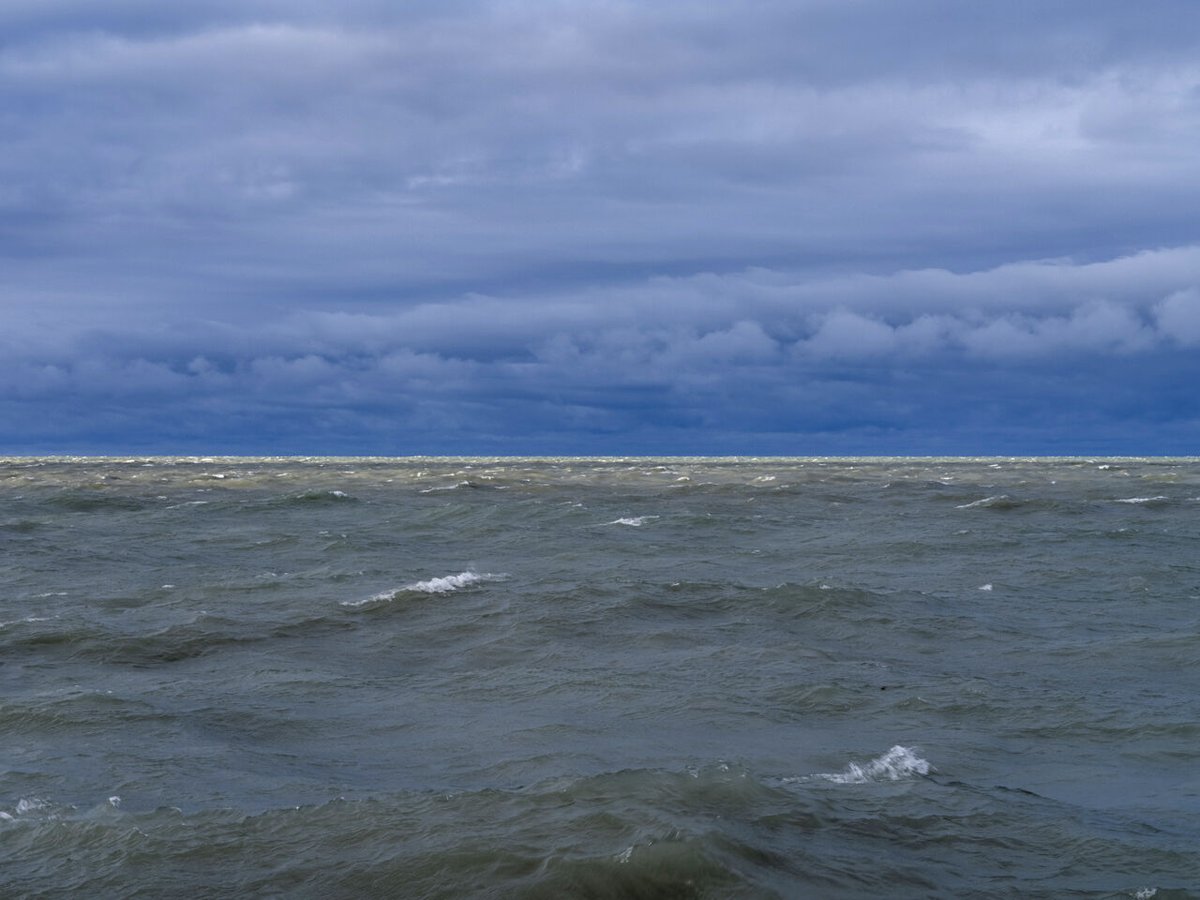Sunlight cuts through heavy storm clouds on April 4th, 2024, illuminating green lake waters filled with waves just starting to build in size.