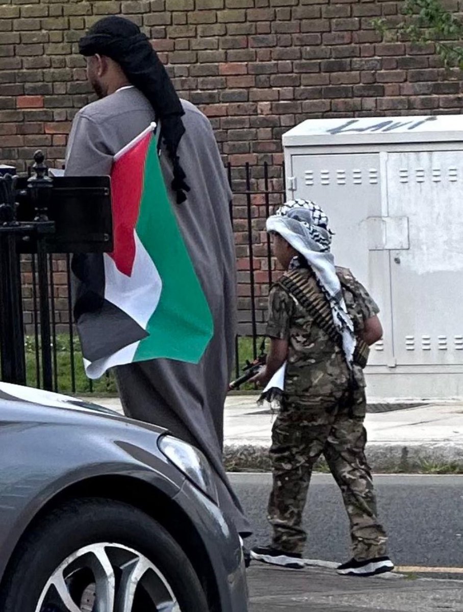 Muslim man holding a Palestinian flag dresses his son as a Hamas terrorist complete with a gun and ammunition in London.