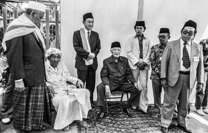 Foto legenda: para pembesar Nahdlatul Ulama, Kiai As'ad Syamsul Arifin, Kiai Ali Maksum, Kiai Masykur Malang, Kiai Idham Chalid, Gus Durrahman Wahid dan Lora Fawaid As'ad di momen bersama menunggu detik-detik kedatangan Soeharto ke arena Muktamar 27 di Pesantren Sukorejo.