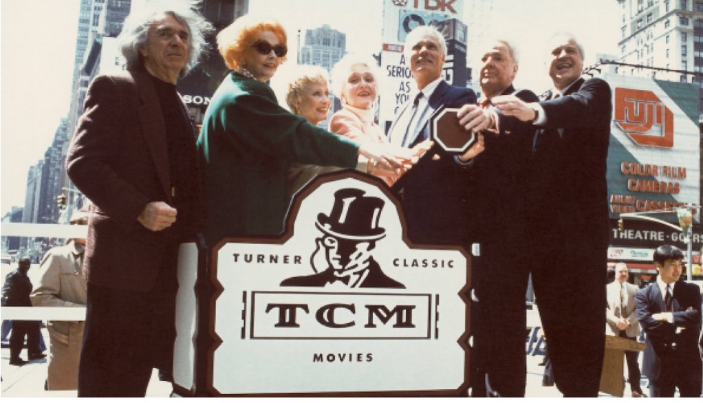 BenMank77's tweet photo. 30 years ago - April 14th, 1994 - Robert Osborne signed @TCM on the air by throwing a big, fake switch in NY.  30 years later, the 5 of us (&amp; this photobombing interloper) are 4 days away from our 15th Film Festival. I’ve also included a photo of me going over my bets on set. https://t.co/P99yKMOwBO