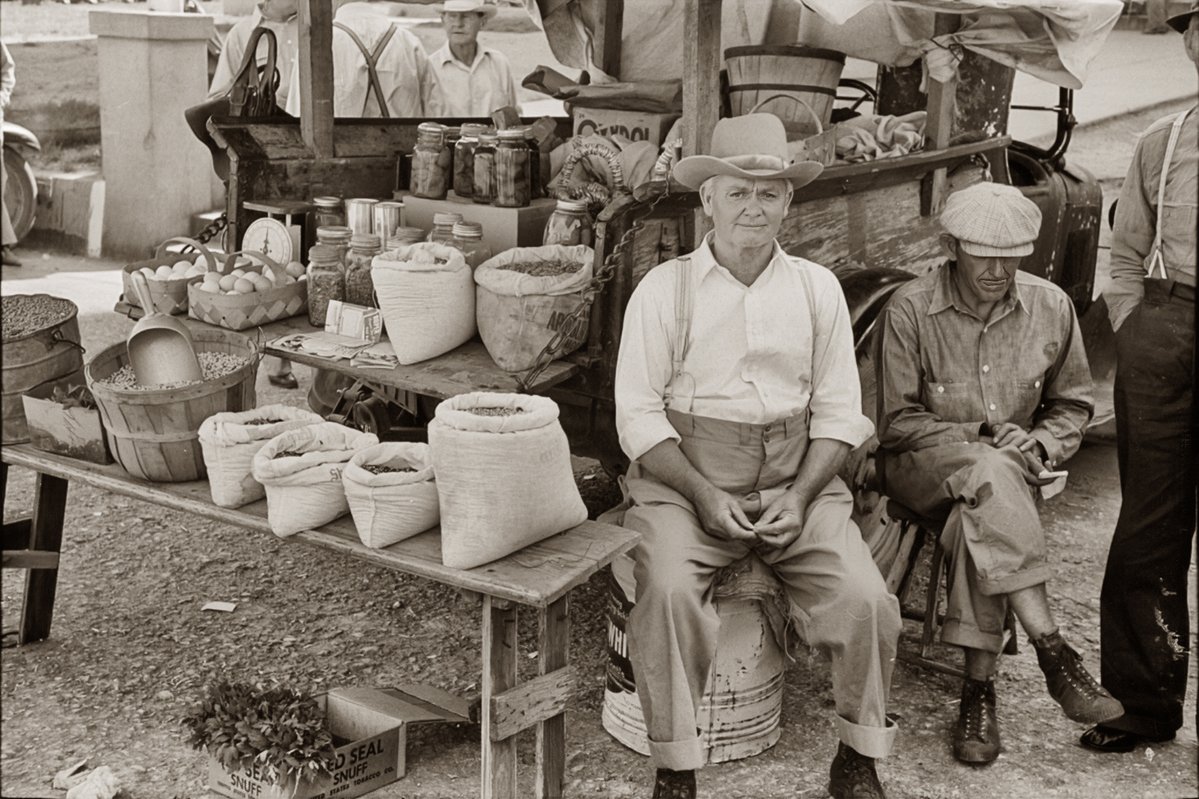 A farmer and his offerings at the Weatherford, Texas Trade Days at the courthouse there in Weatherford, 1939. He has a kind face, I think. I also think he took the time to put on his nice clothes before going into town, as many folks did back then. Taken by Russell Lee.