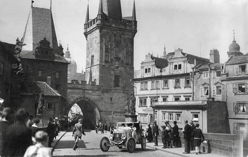 1922-27 Aloha Wanderwell, stops on the Charles Bridge, “The Karlsbrücke” in Prague, for a photo of her and the Model T Ford. A crowd gathers as Cap sets the scene. Beautiful historical city of statues, spires, towers and buildings. Amazing Adventures. AlohaWanderwell.com RDT