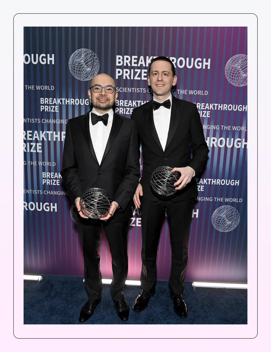 Isomorphic Labs' CEO Demis Hassabis is standing with John Jumper from Google DeepMind. Both are wearing formal clothing and are smiling at the camera whilst holding their Breakthrough Awards for Life Sciences.