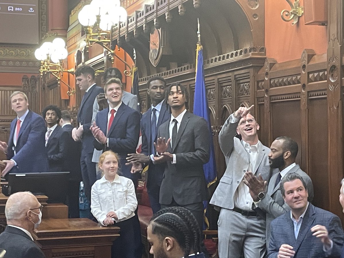 UCONN men’s basketball team watches video of championship team in CT House chamber; Coach Hurley points to video screen