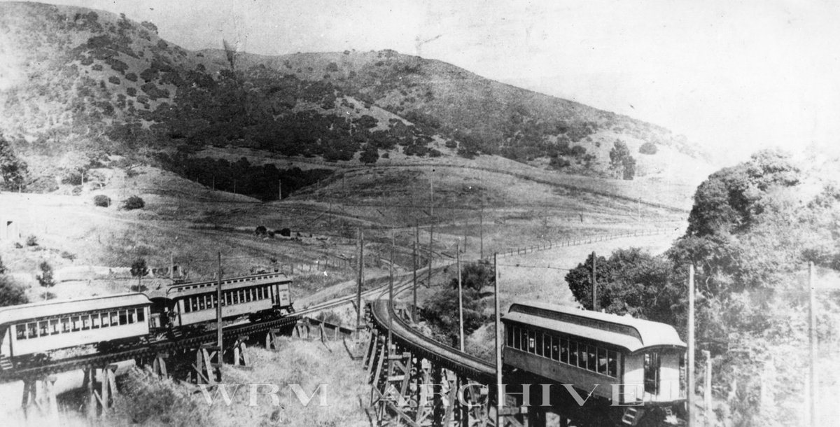 Rumbling over the Lake Aliso Trestle, a two-car California Ry train heads east from Leona Heights towards the switchbacks to Mills College, passing by car #21, stored on the bridge.

Built by Carter Bros. in 1895, #21 is best remembered today as our Key System #1201.

c. 1895