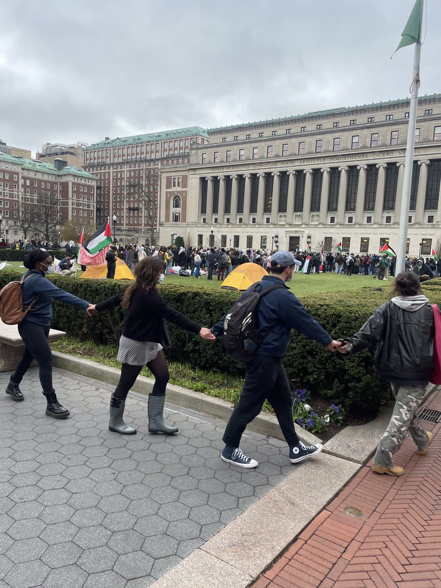 Earlier today, Columbia University called in the NYPD to clear a student encampment from the East Lawn and arrest the students, but other students have now set up a new encampment on the opposite lawn and linked hands around it. In the background is Butler Library.