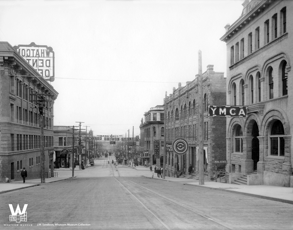 Step into 1910 with J.W. Sandison's lens! Explore Holly Street's history—YMCA, Pike Building, Sunset Building. Pike's sandstone lives on in Whatcom Falls Park. Exchange Building, Hotel Henry, YMCA. Remembering Alaska Building's fiery end in 1969. #TBT #Bellingham #WhatcomMuseum