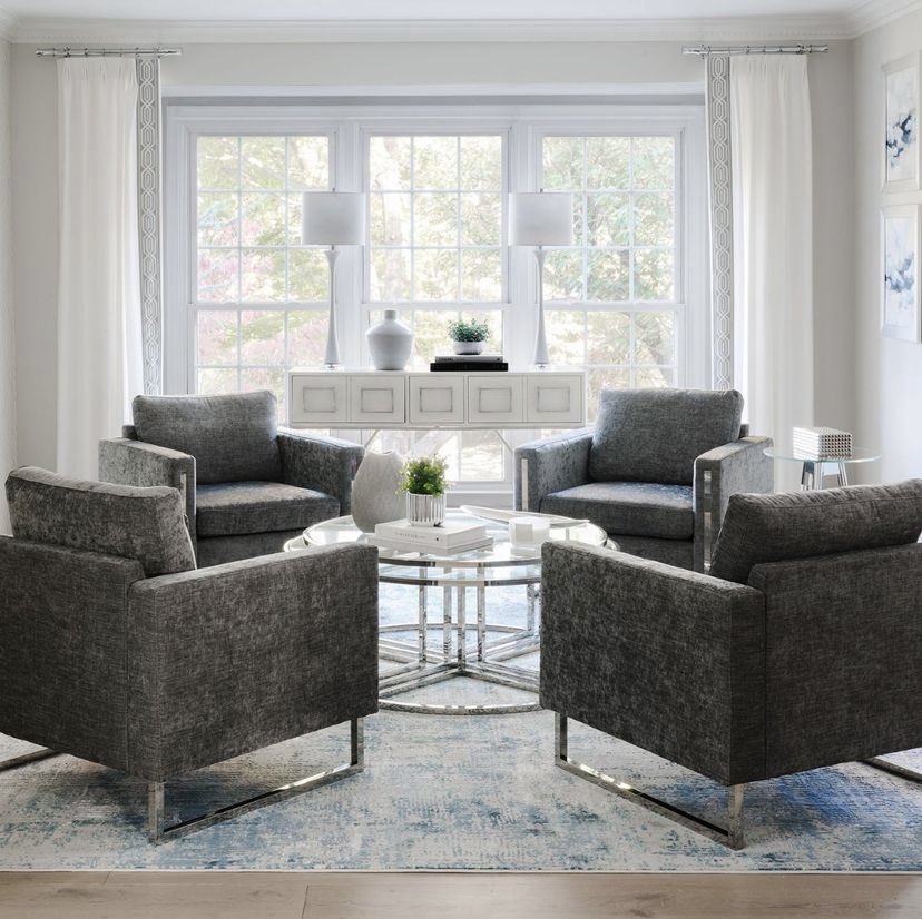This modern glam living room boasts grey fabric, chrome-accented lounge chairs, giving comfort and symmetry. The large chrome and glass cocktail table adds a wow factor, while the blue and grey rug brings pattern and color! ✨ #InteriorDesign #HomeDecor #LivingRoomDesign