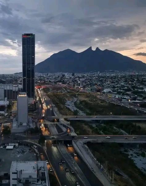 Así la tarde en Monterrey, NL, México. View the image to see an expansive cityscape at dusk, with a multi-lane highway, tall buildings, and a majestic mountain range as the backdrop. #Monterrey #Cityscape #Nature #Twilight