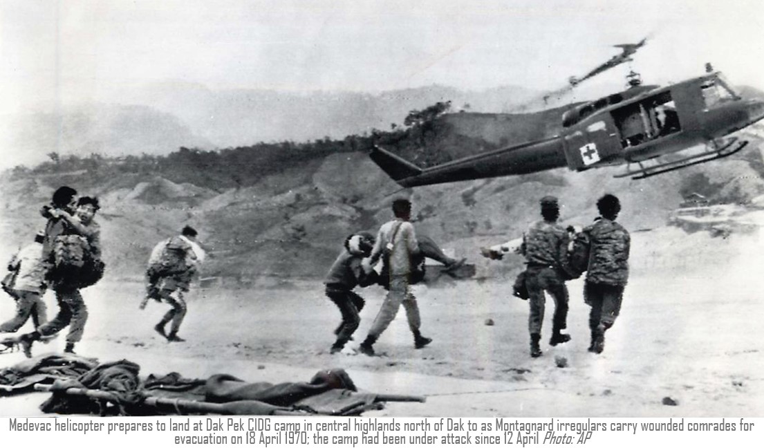 Medevac helicopter prepares to land at Dak Pek CIDG camp in central highlands north of Dak to as Montagnard irregulars carry wounded comrades for evacuation on 18 April 1970; the camp had been under attack since 12 April