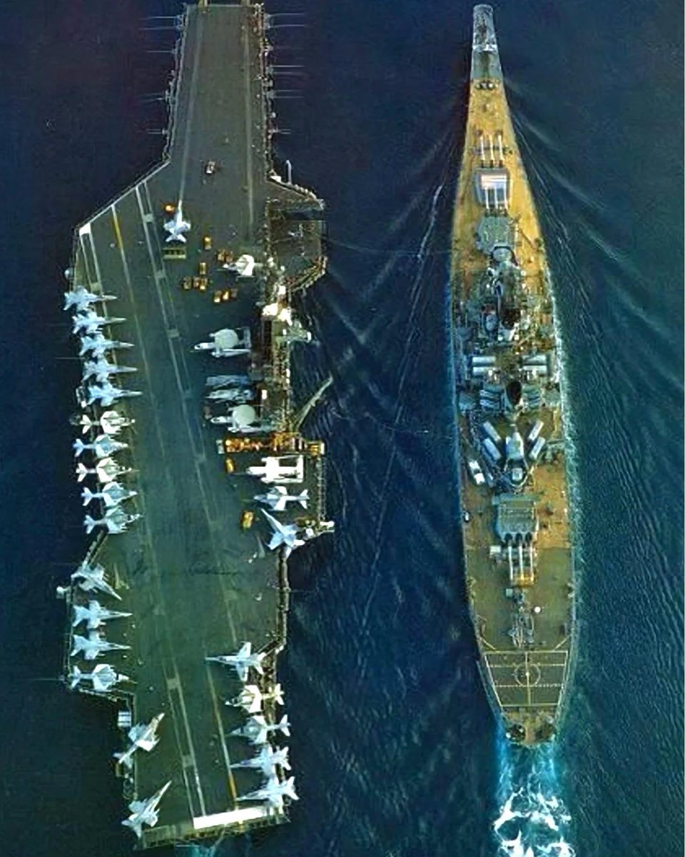 A Midway Class US aircraft carrier next to an Iowa Class battleship sometime in the late 1980s.