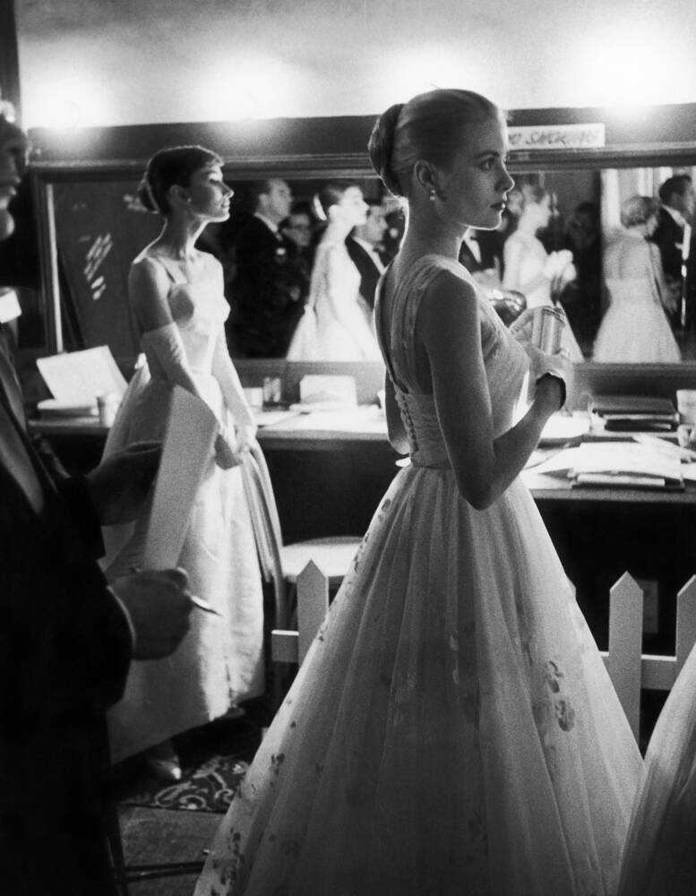 @fasc1nate The image depicts Audrey Hepburn and Grace Kelly, two iconic Hollywood actresses, standing together and waiting backstage at the RKO Pantages Theatre during the 28th Annual Academy Awards in Hollywood in 1956. The photo is in black and white, and both actresses are dressed in