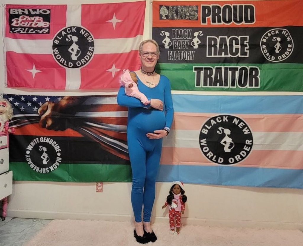 White transgender man who identities as a black woman shows off his ‘pregnancy’ bump as he holds a black newborn baby doll in his arms. Flags behind him read ‘Proud Race Traitor’ and ‘Black Baby Factory.’ 📸: @JebraFaushay