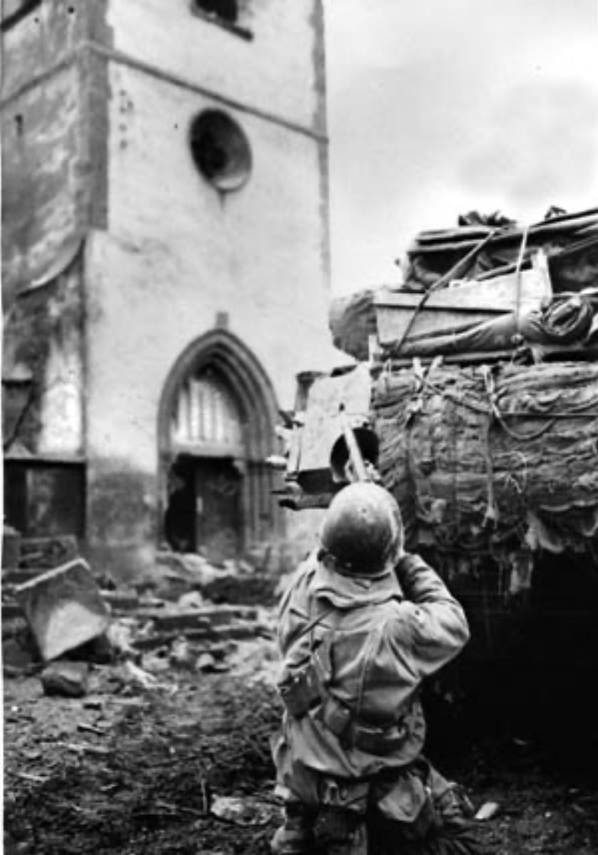 During the 1st weeks of 1945, an American soldier uses a tank as a shield as he fires on a German sniper holed up in a church in the village of Oberhoffen-sur-Moder, southeast of Haguenau, France. 🪖
