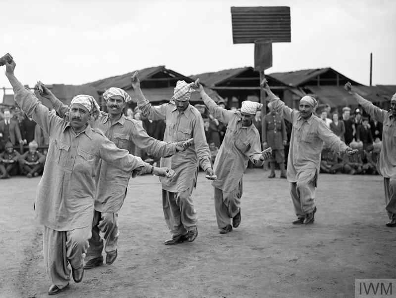 To pass time while stationed in peaceful France, troops of the British Expeditionary Force watch a Punjabi dance from Indian mule-handlers, attached to British army as an Animal Transport Company.