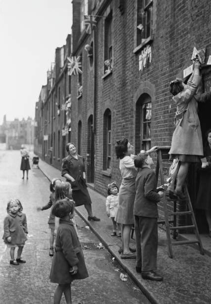 A photograph of Residents of a house in Barbel Street, Lambeth attaching flags and decorations above their front door as they celebrate Victory in Europe Day (VE Day) taken on the 8th May in 1945.