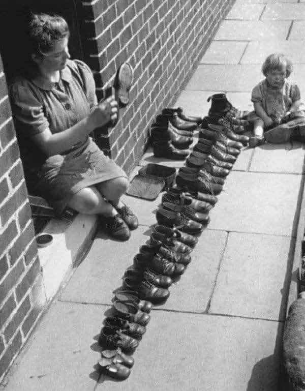 A photograph of a mother cleaning her large familys shoes in London in 1945