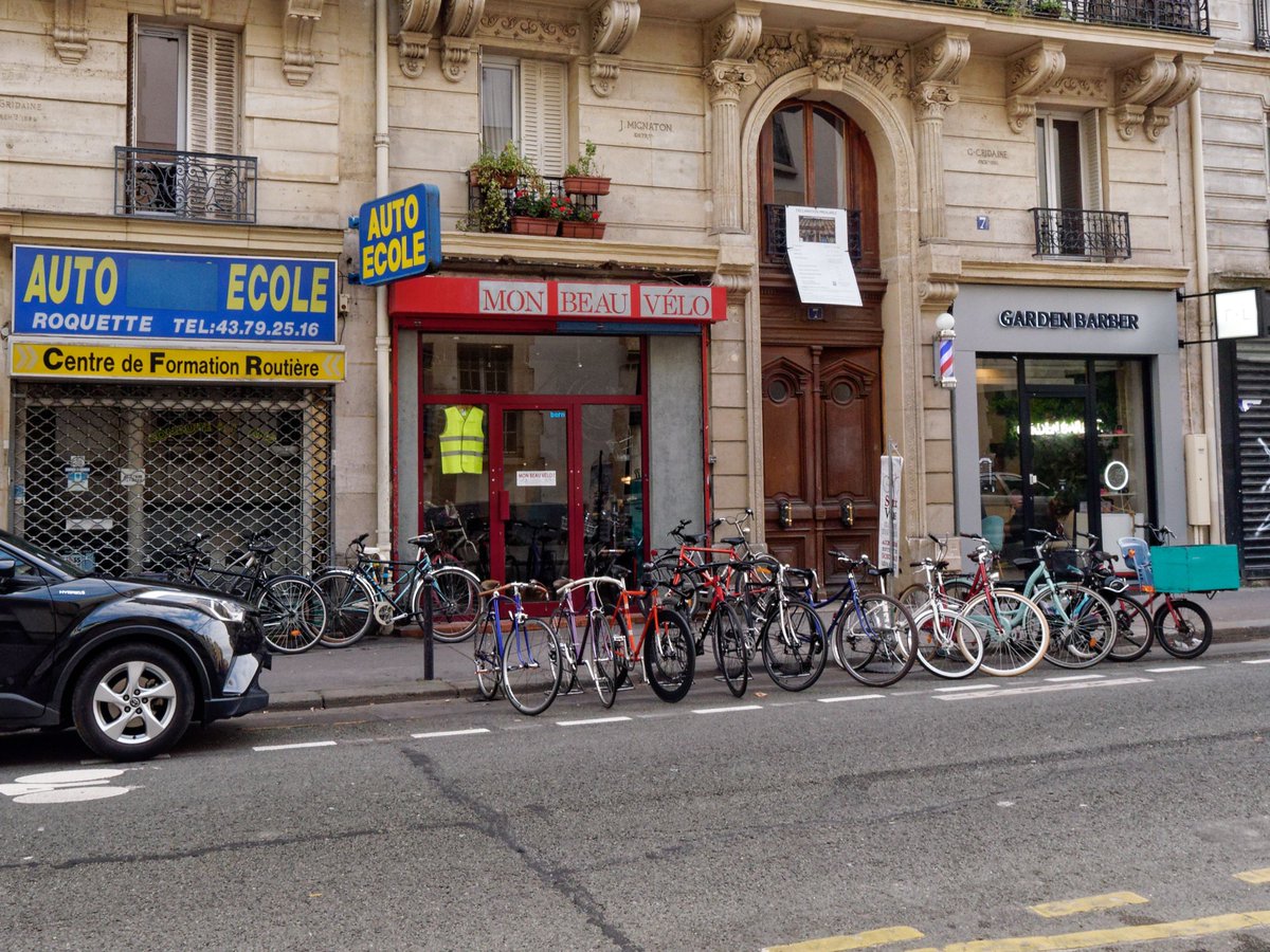 Trois générations de boutiques parisiennes: l'auto-école ancienne, la boutique vélo apparue il y a une petite dizaines d'années, et le barbier qui vient d'ouvrir.