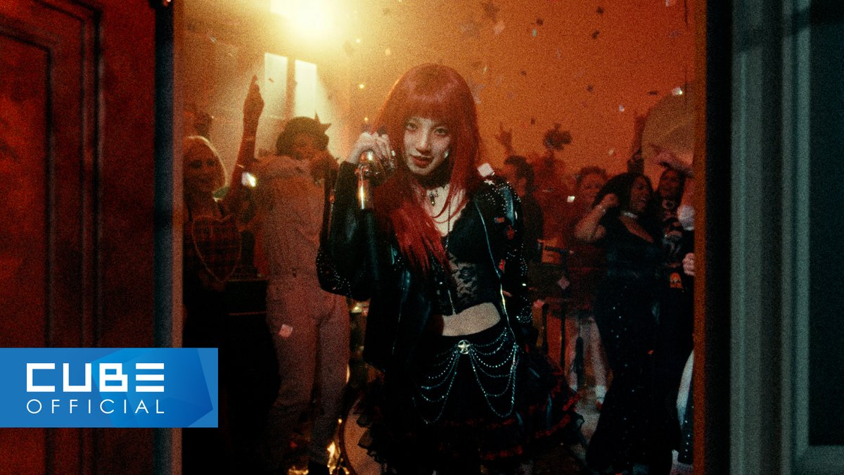 A music video scene featuring a woman with bright red hair holding a microphone in a dark, red-lit club setting, with a 'CUBE OFFICIAL' logo in the corner.