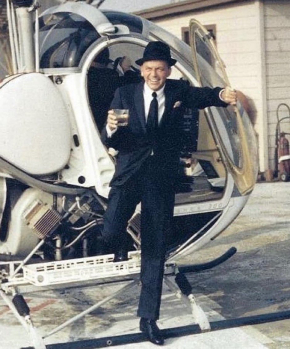 Frank Sinatra stepping off of a helicopter with a drink in his hand, 1964.