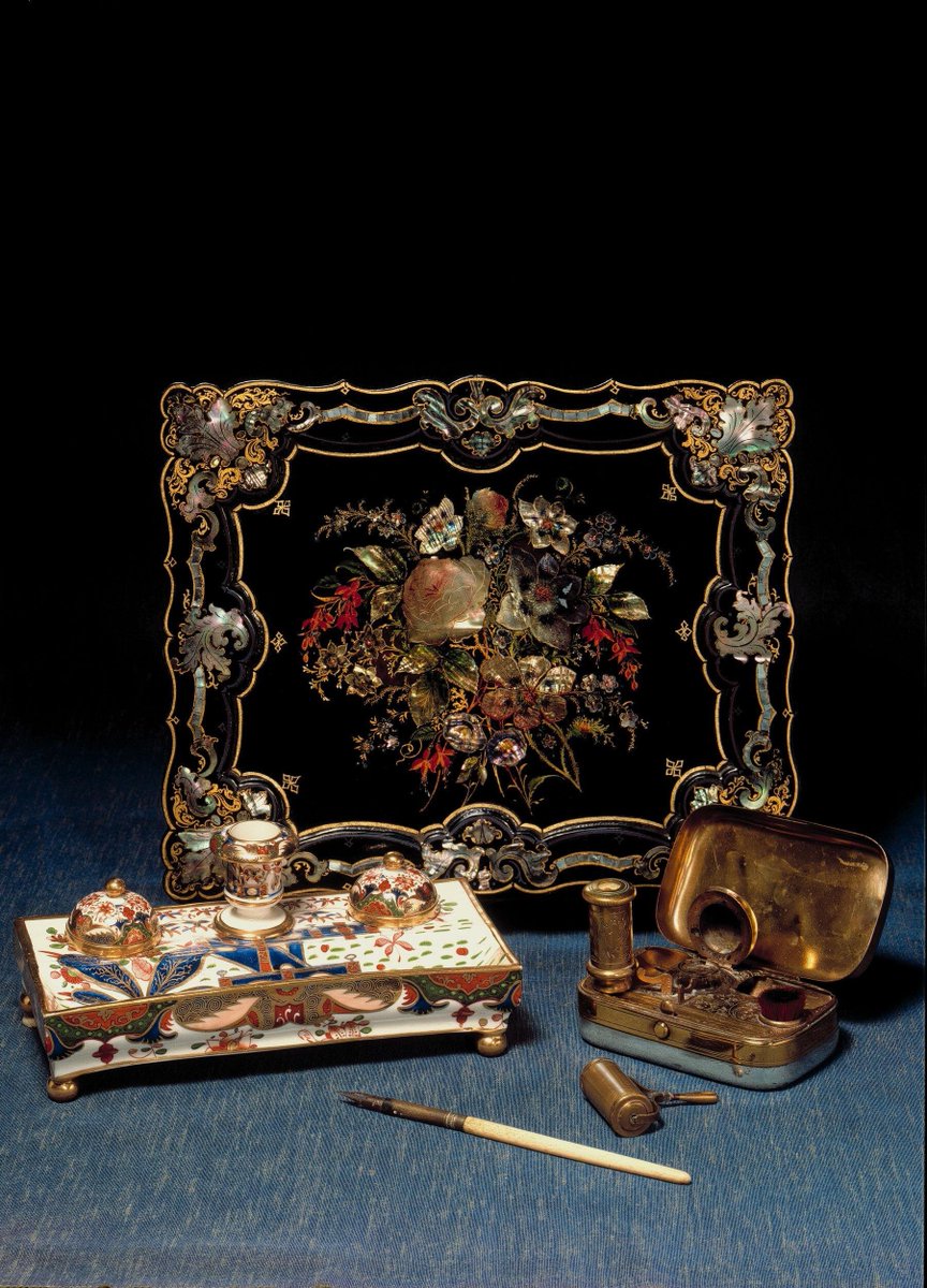 Writing box in papier-mâché, with stationary compartments, pen tray and inkpot, painted and inlaid with mother-of-pearl on the lid. English, 1840-70. Victoria & Albert Museum.
