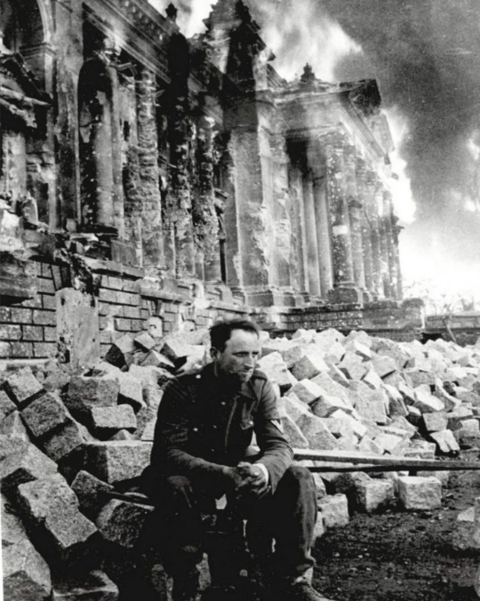 A defeated German soldier sits in front of a burning Reichstag in Berlin in May, 1945. #History #WWII