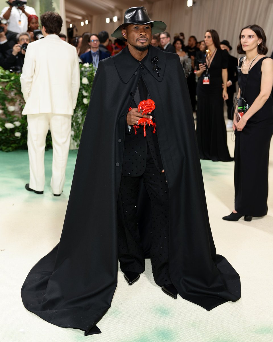 .@Usher arrives at the 2024 #MetGala wearing custom-made Alexander McQueen by Seán McGirr. ​ #Usher wears a custom-made cape with black dipped rose appliqué detail, a tuxedo jacket and trousers in black with all-over jet stone embroidery and red dipped rose appliqué detail.