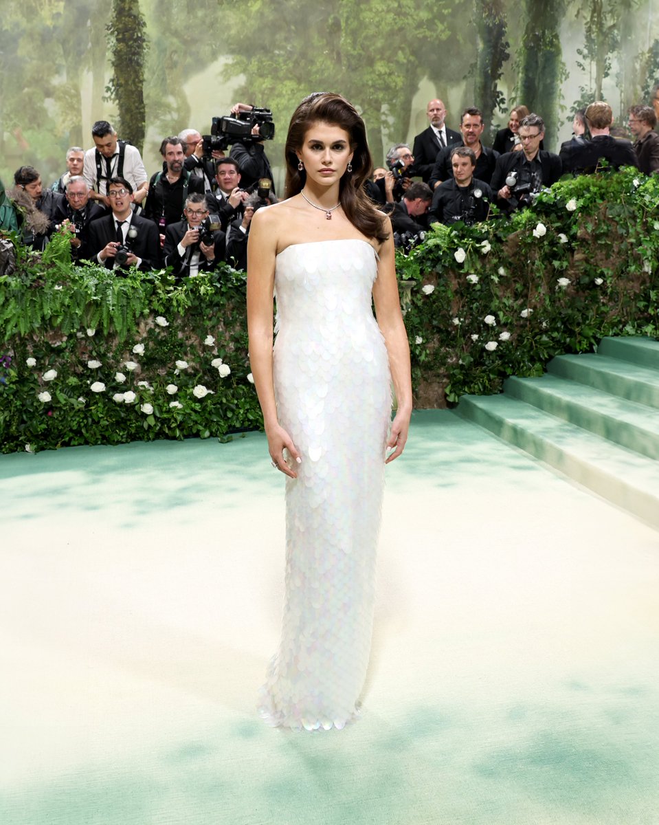 Kaia Gerber attending the 2024 Costume Institute Gala “The Garden of Time” at the Metropolitan Museum of Art. Kaia Gerber wore a strapless dress featuring all-over embroidered white iridescent sequins inspired by the Fall/Winter 2011 collection, paired with silver sandals.…