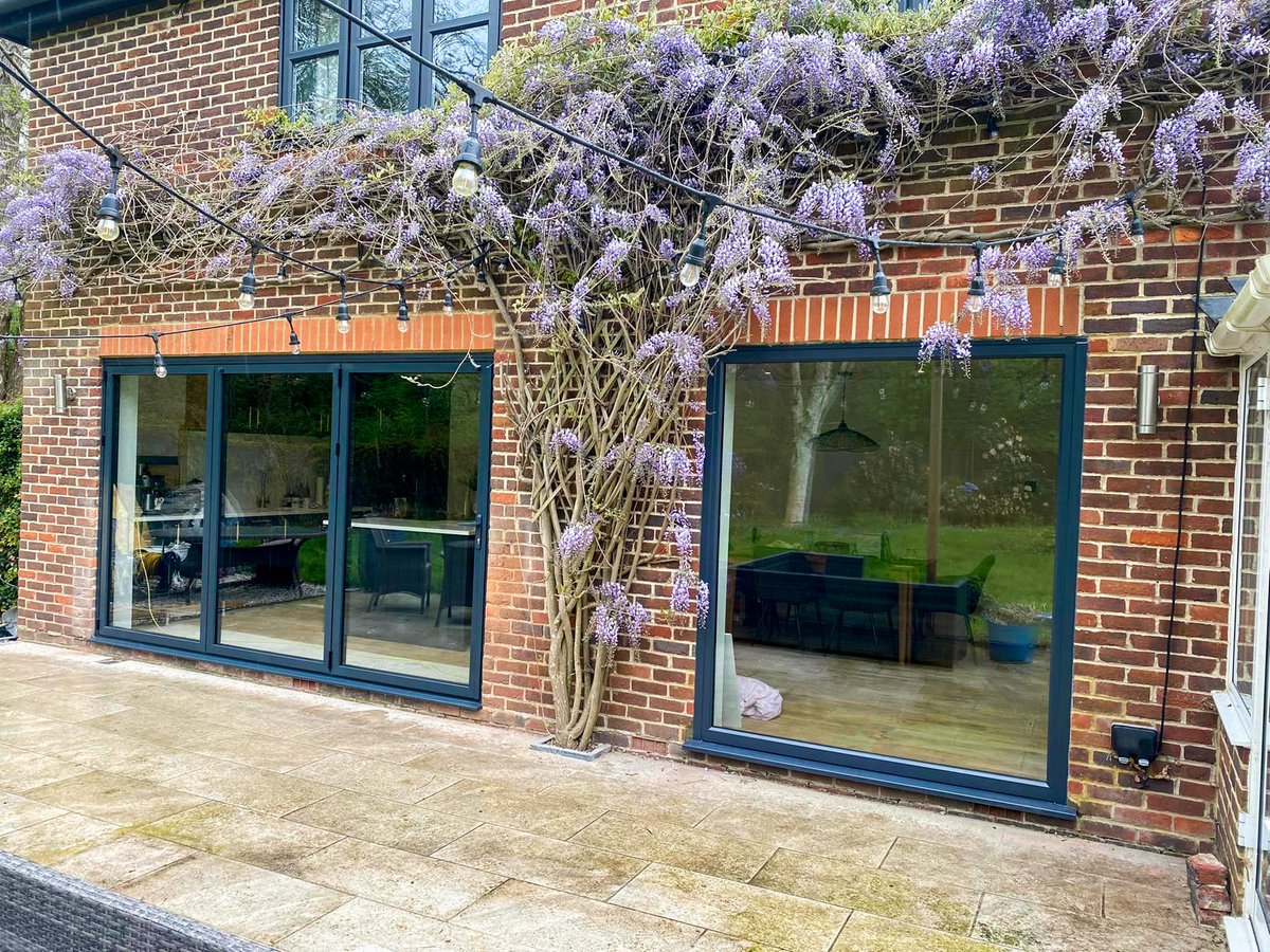 Dreaming of bringing the outdoors in? This beautiful patio with it's falling wisteria, festoon lighting and new Korniche Bi-folding Door is total #patiogoals! The perfect space for entertaining & relaxing! #Korniche #BifoldingDoors #bifolddoors #PatioDoors #AnthraciteGrey