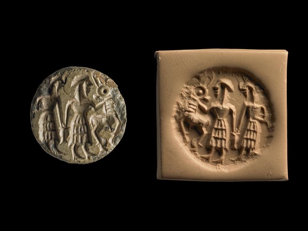 This steatite Stamp seal of the Dilmun type (2000-1800BC) was found at Ur by Leonard Woolley and depicts two men. The two men clutch a jar between them while one holds a gazelle by the neck.