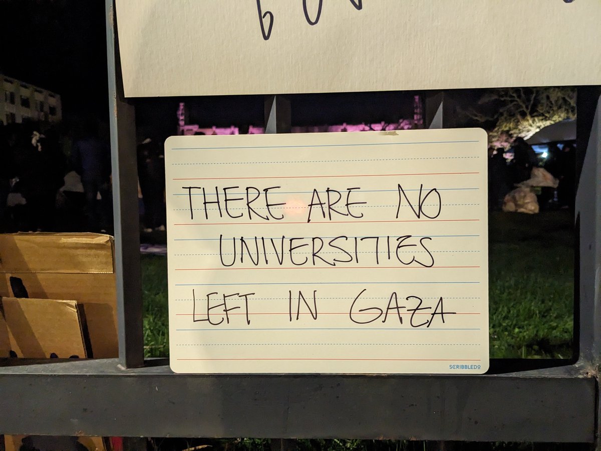 A sign on the fence reads, 'THERE ARE NO UNIVERSITIES LEFT IN GAZA'