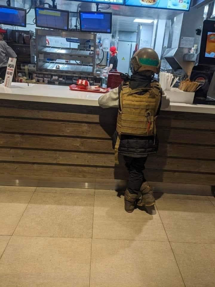 Kid in a bulletproof vest waiting for his KFC order, Kharkiv, Ukraine.