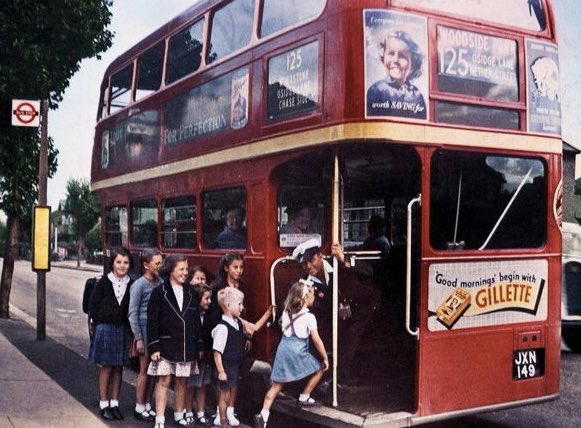 A group of young school children are helped onto a bus by the conductor. North London, c. 1949