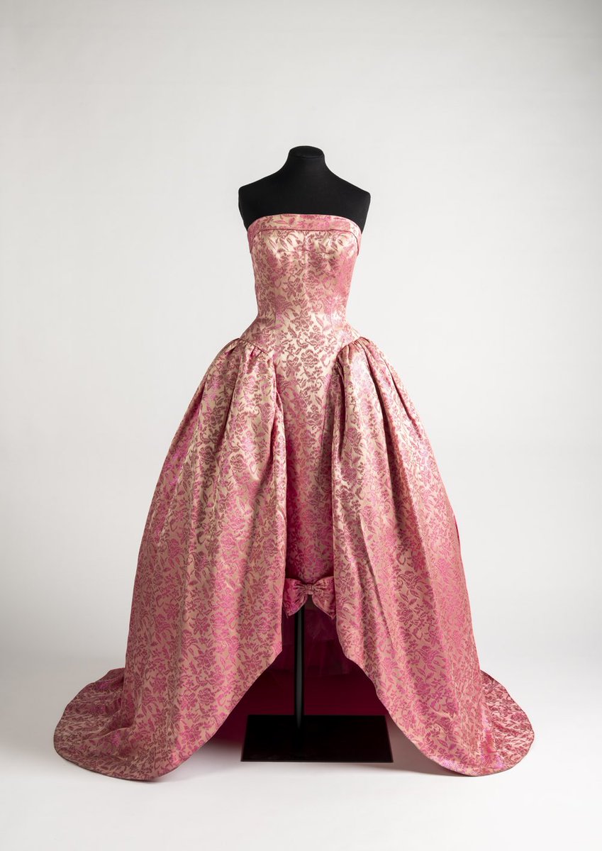 British designer John Cavanagh brought all of the rococo flair to this late #1950s evening dress, paniers swooping from either hip and a rosy bow adorning the skirt. It demands a balmy early summer evening with a long cool drink and twilight birdsong on the air @Fashion_Museum