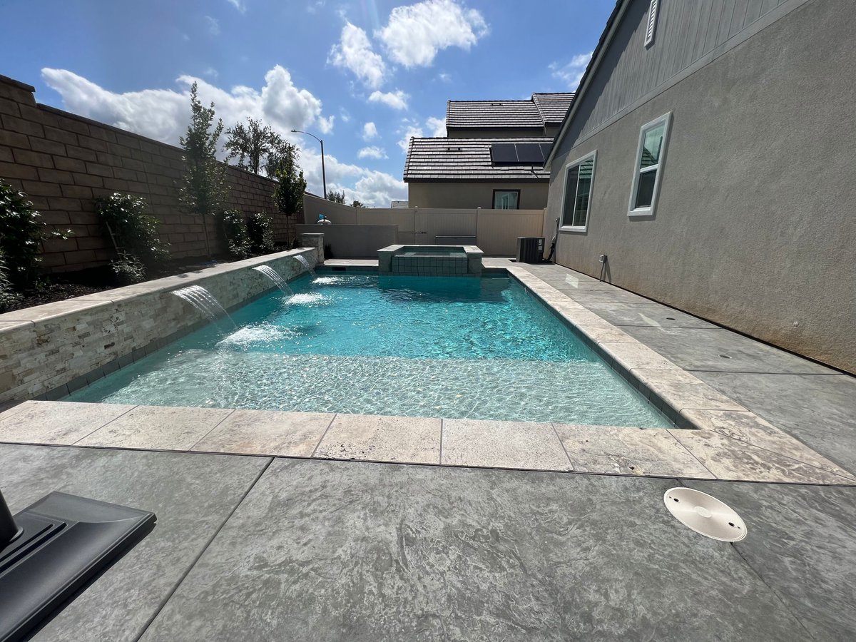 Don't let  limited space get in the way of your oasis. Featuring a pool with a reef step, pebble tech finish, concrete coping, and colorful lighting, this backyard turned out perfect for summer fun. Contact us today  #BackyardDesign☀️