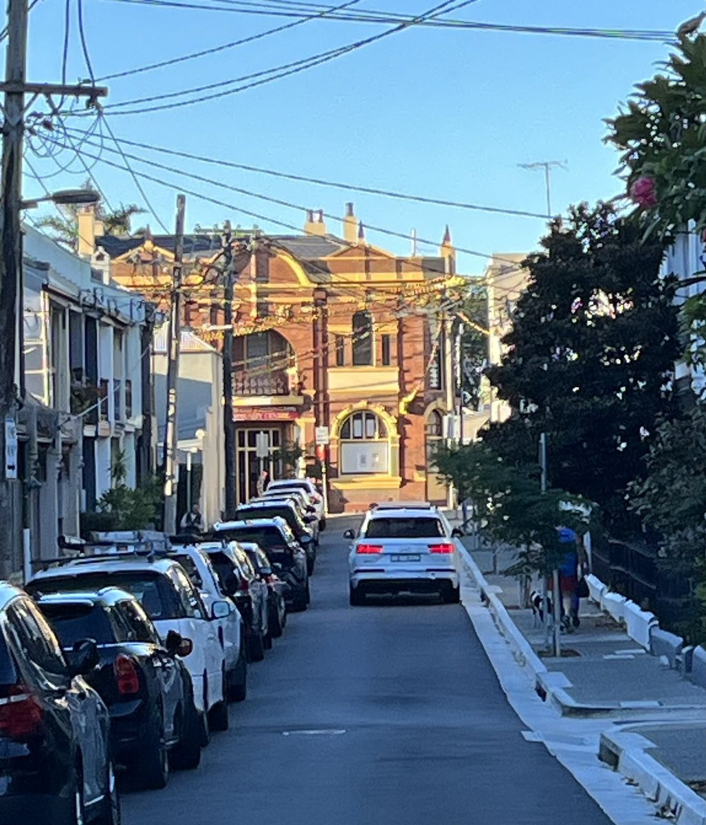 Sunny Streetscene; 
George St Paddington.
#sydneyterracehouses on both side, close with wires & poles to left, setback with front gardens & new street trees to right.
Vista closed by civic architecture at end
#publicsydney