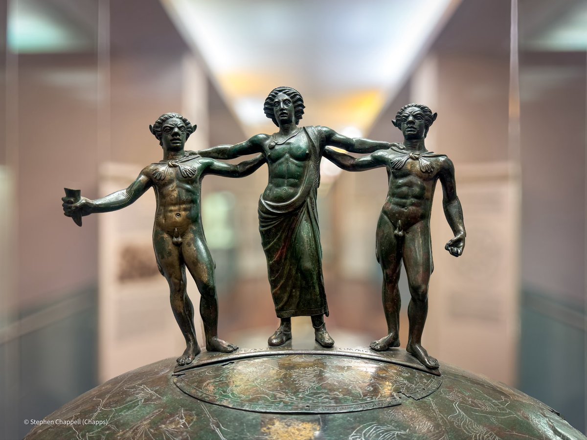 Bronze sculptural handle of the Ficoroni Cista, depicting a bulla-wearing Dionysus and two companion satyrs, bro-ing it up. Cistas are cylindrical metal boxes with engraved scenes on their barrels, and decorative handles and feet, and were used for storing women’s items.  1/