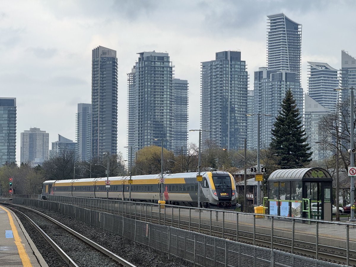 A VIA Charger/Venture train departing TMC for Toronto Union, with the towering Humber Bay Shores community in the background.