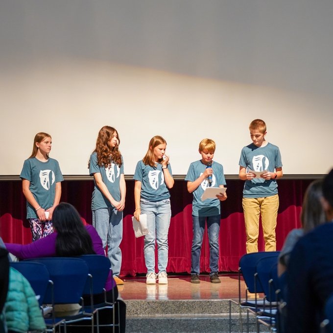 Five middle school students stand on stage and share learning reflections