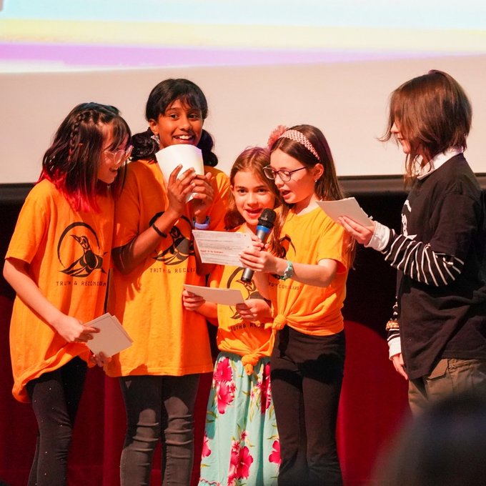 Five elementary students stand near mic during presentation on stage